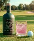 Bottle of Mulligin gin with a glass of pink cocktail and golf ball on a golf course.